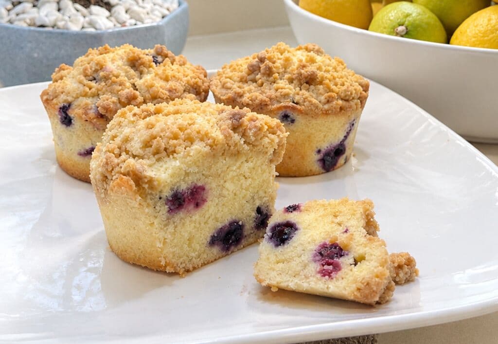 Muffins de arándanos con streusel en un plato blanco, uno partido mostrando la fruta